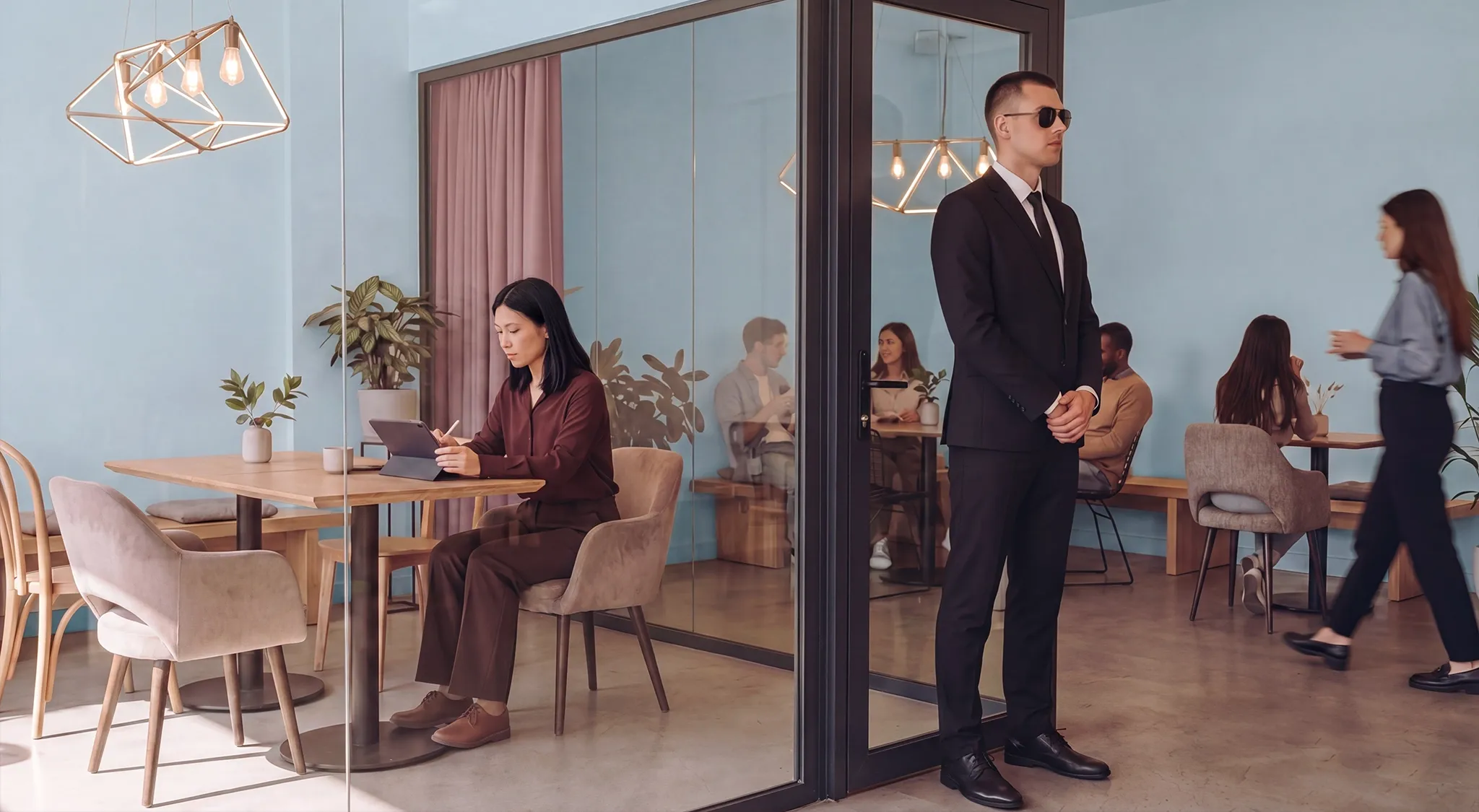 Remote Work Security: A woman working with her laptop in a private space with a bodyguard at the door
