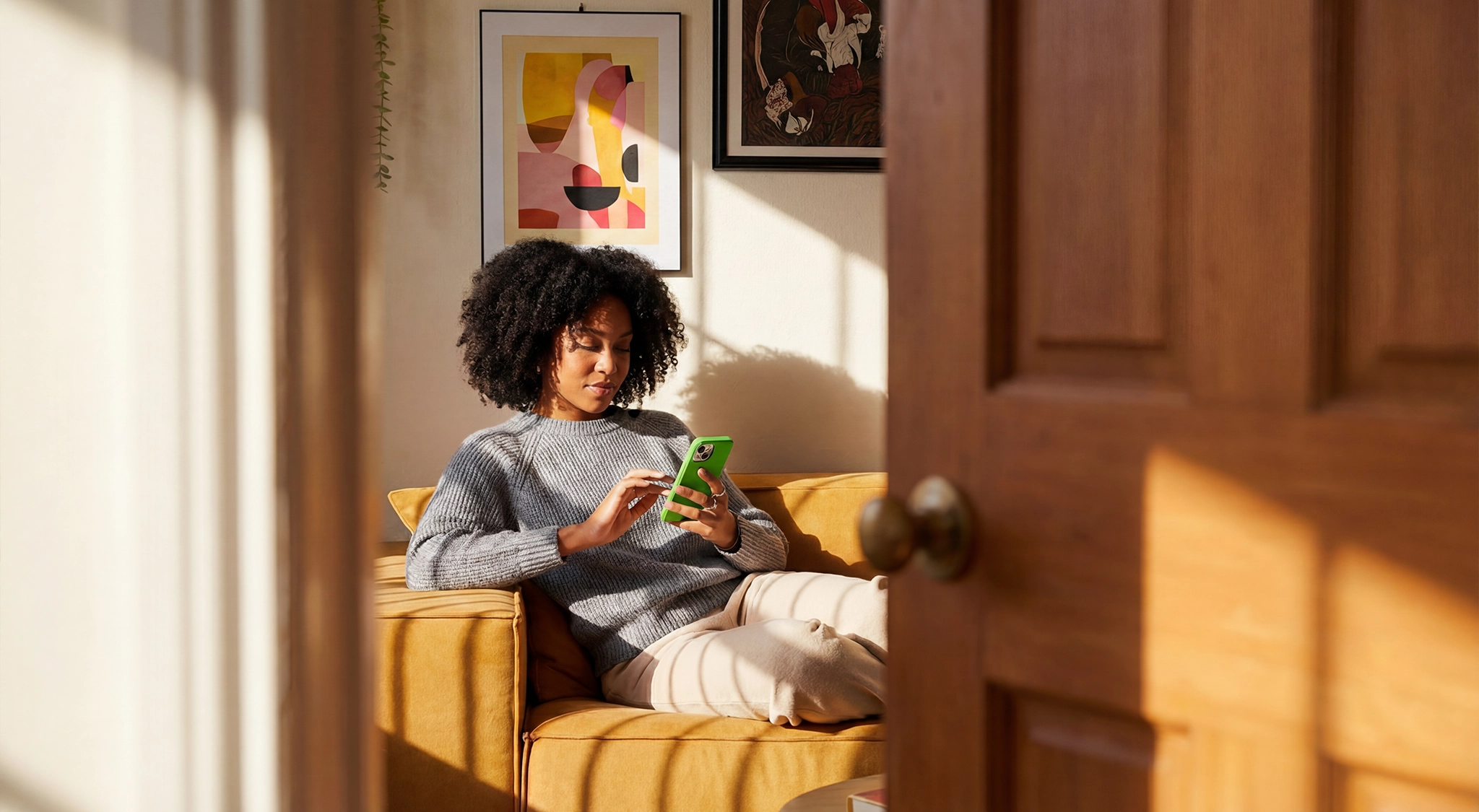 A girl lying on a sofa in a room. She's working with her cell phone