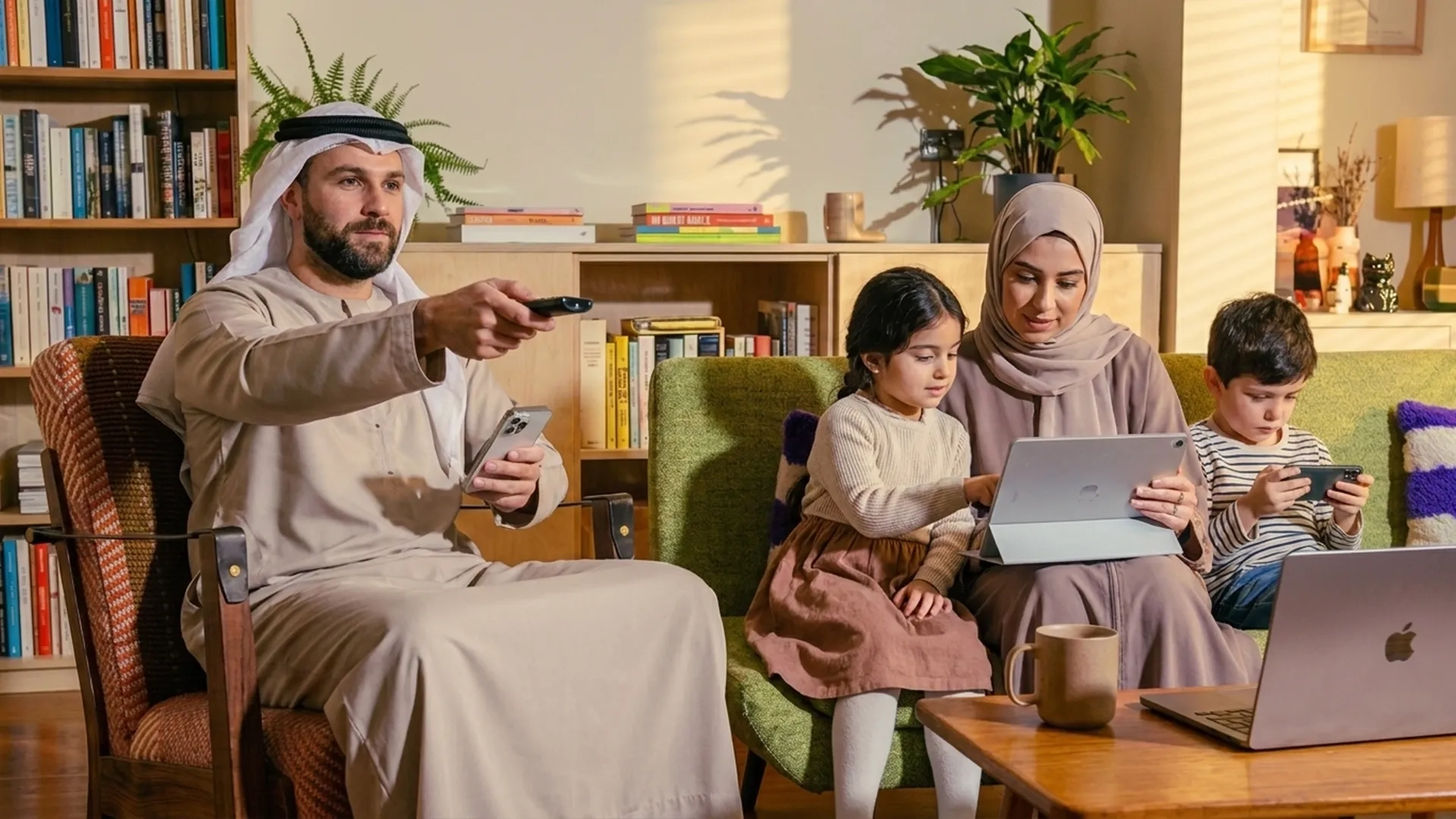 An Arab family sitting on a sofa and working and playing with their gadgets and electronics